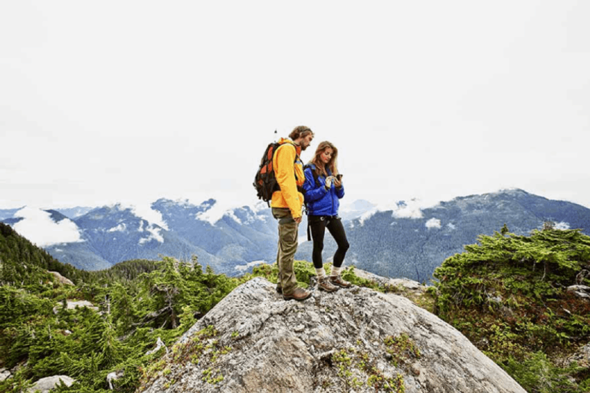 two people on a mountain top looking at a hand-held mobile device